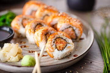 Baked sushi maki rolls with salmon, crab and spicy sauce on a plate with chopsticks, soy sauce, wasabi and ginger. Japanese traditional fish food closeup served for lunch in modern gourmet restaurant