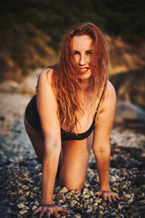 A close-up portrait of a girl with red hair and an open neckline as a predator moves along a wild beach.