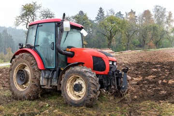 Red tractor on a muddy field. Agricultural work. Autumn foggy morning on the farm. Agriculture machinery.