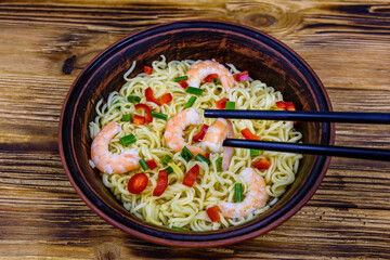 Instant noodle with shrimps, red pepper and green onion in a ceramic bowl. Japanese food. Chopsticks with shrimp