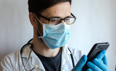 A young handsome doctor wearing glasses and a medical face mask provides a patient with a video...
