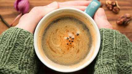 A men's hands are holding a cup of aromatic coffee. A cup of aromatic coffee stands on a wooden table. An aromatic coffee with foam. Invigorating coffee with delicious milk foam.