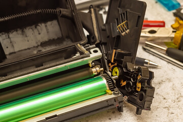 a worn out disassembled laser printer cartridge is lying on the service center table next to the tools