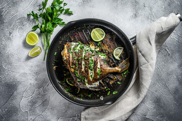 Grilled John Dory fish with lime and parsley in a pan. Gray background. Top view. - obrazy, fototapety, plakaty