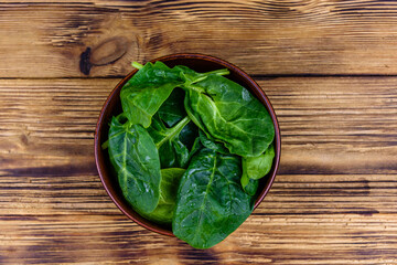 Ceramic bowl with spinach leaves on rustic wooden table. Top view