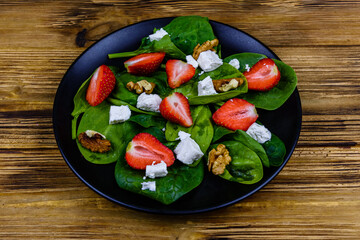 Salad with spinach leaves, feta cheese, walnuts and strawberry on a black plate