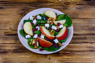 Salad with spinach leaves, feta cheese, cranberries, walnuts and apple in a ceramic plate