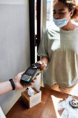 Close up of hand of man holding payment terminal while woman paying using credit card. She is...