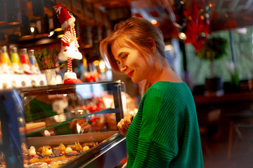 Young pretty woman looks at the windskreen with cakes of eating something tasty in cafe on New Year's Eve holidays