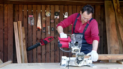 Male joiner processes wood bar using a miter saw in a workshop. Work with miter saw for cutting boards and bars. Home renovation with professional construction and repair tool.