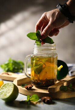 Hot moroccan tea with hand. Drink with lemon, lime, orange, mint, badian and cinnamon in a transparent jar on wooden board. Sunlight. Tropical fruit. Background image, copy space, lifestyle