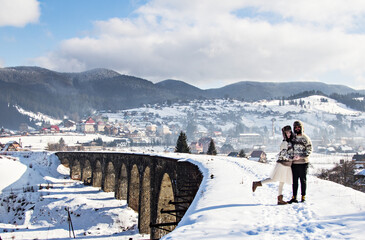 winter love story. guy and girl, man and woman in knitted sweaters walk on an old bridge in the mountains