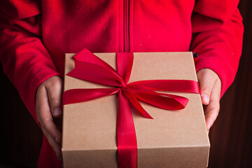 Gift box with a red bow in the hands of a child in a red sweater.