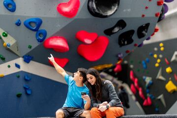 A young woman and man using mobile phone in a climbing gym.