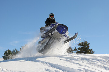Fototapeta na wymiar extreme snowmobile rider jumping machine through powder in mountains