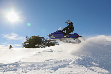 extreme snowmobile rider jumping machine through powder in mountains