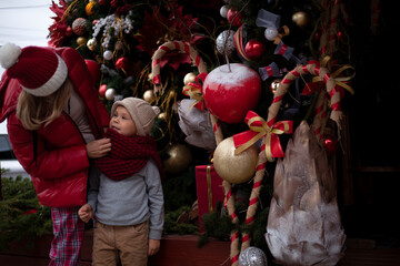 Obraz premium Happy family, young pretty woman with child spend time together outdoor at the background decorated christmas tree with lights garland on New Year's Eve holidays. 
