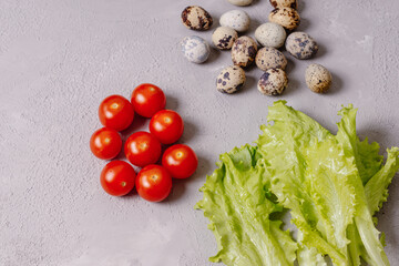 Cherry tomatoes, quail eggs and lettuce leaves on gray background