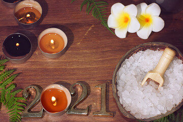 Top view of spa composition with white sea salt plumeria flowers and numbers 2021 illuminated by burning candles