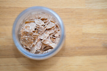 Multigrain brown flakes for breakfast  in a glass jar on a wooden oak table background top view. Ideas for storing bulk food, cereals at home in the kitchen.