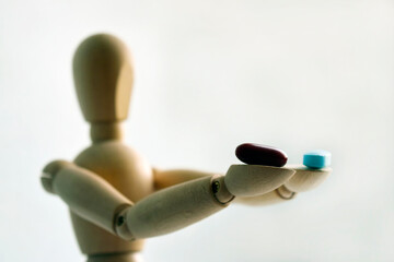 Wooden figurine of a man, holding two pills, on a light background with free space for your text. Medicine and healthcare concept.