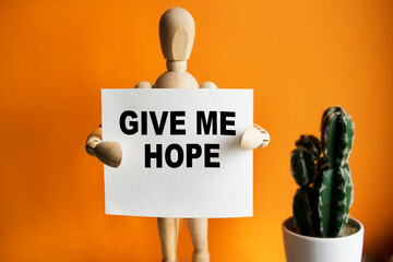 The wooden man holds a white sign with the text GIVE ME HOPE in his hands. The content of the...