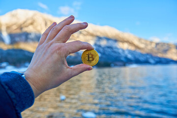 Man&rsquo;s hand holding golden Bitcoin on mountain background
