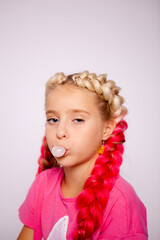 a cute girl in bright multicolored clothes and with colored braids blows bubbles from gum