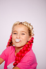 a cute girl in bright multicolored clothes and with colored braids blows bubbles from gum