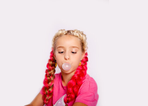 a cute girl in bright multicolored clothes and with colored braids blows bubbles from gum
