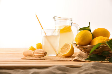 Jug and glass with lemonade on table and sand