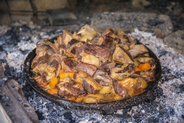 Traditional specialty of lamb and vegetables prepared under a baking bell in earthware on fire