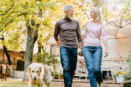 Happy Senior European Couple Walking Their Dog In The City Park In Autumn