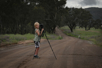 Little boy outdoors in pretty country location taking photos with dslr full frame camera on tripod