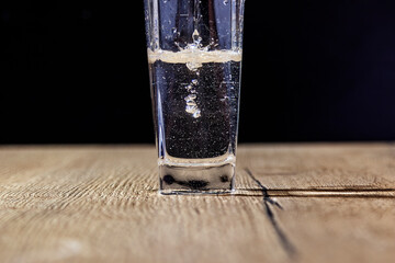 water is poured into a glass on a wooden table with a black background close-up