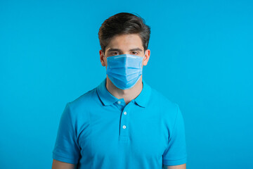 Portrait of handsome man in medical mask looking to camera. Guy in studio on bright background. Coronavirus, covid-19, epidemic reality concept.