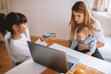 Mother using a computer and holding her baby. Cute daughter helping her mother.