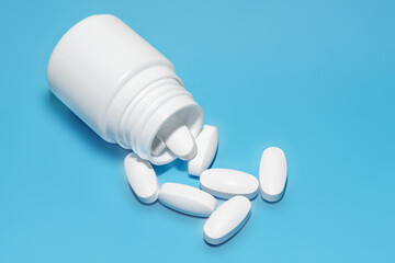 White tablets scattered from a plastic bottle on a blue background. Top view with copy space.