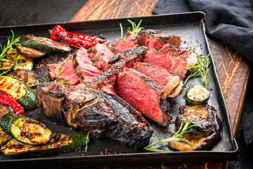Traditional barbecue dry aged wagyu porterhouse beef steak offered with paprika and eggplant as close-up on a rustic metal tray