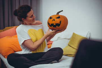 Beautiful caucasian woman making Halloween decoration, holding big pumpkin with painted face on