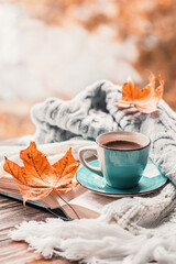 Autumn morning coffee. A cup of coffee on a wooden table and a warm sweater on a background of autumn leaves. Still life concept. Copy space.