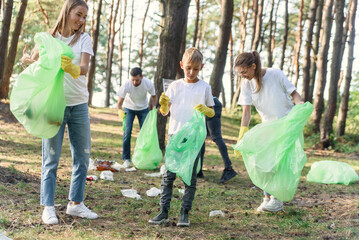 Naklejka na ściany i meble Active team of international naturalists in white t-shirs collecting rubbish into plastic packs at forest.