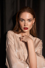 Closeup studio portrait of young beautful pretty caucasian woman with red haie and red lips posing against black curtains. Fashion trendy shoot