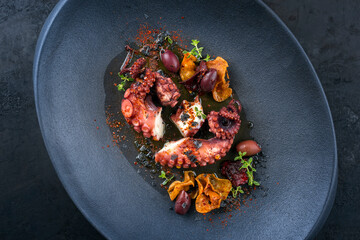Modern Style traditioneller italienischer Polpo alla Griglia mit with gegrillten Oktopus, Oliven und Gemüse Chips angeboten als close-up auf einem Design Teller mit Textfreiraum © HLPhoto