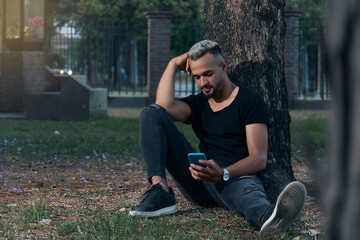 young latin man sitting in the park with a cell phone in his hand