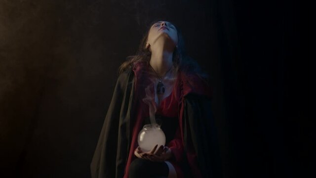 Young witch with glass ball with smoke, slow motion