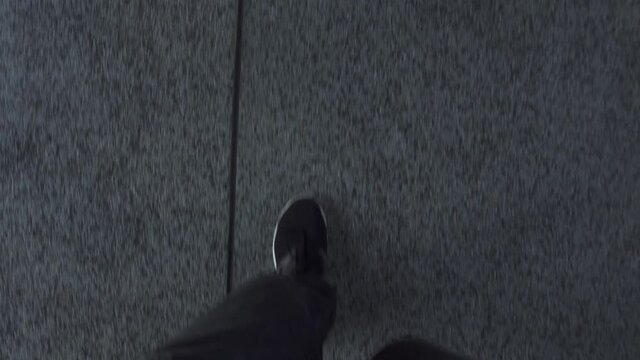 Young person wearing grey sports pants with black soft sneakers walks along road with light grey stone tiles on contemporary city street first point view.