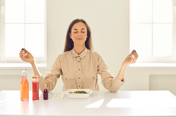 Happy relaxed woman meditating before meal during lunch break at home or in office