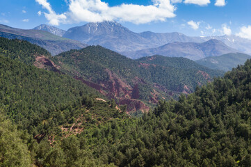 Fototapeta na wymiar Landscape with slightly snowy mountains and blue cloudy sky in the Morocco Atlas Mountains in summer in the fertile Ourika Valley near Marrakech, Morocco