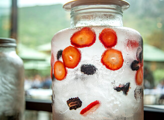 Glass container filled with ice water and fruit such as strawberries and blackberries
